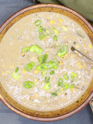 Vegan corn chowder in bowl with scallions garnish and spoon.