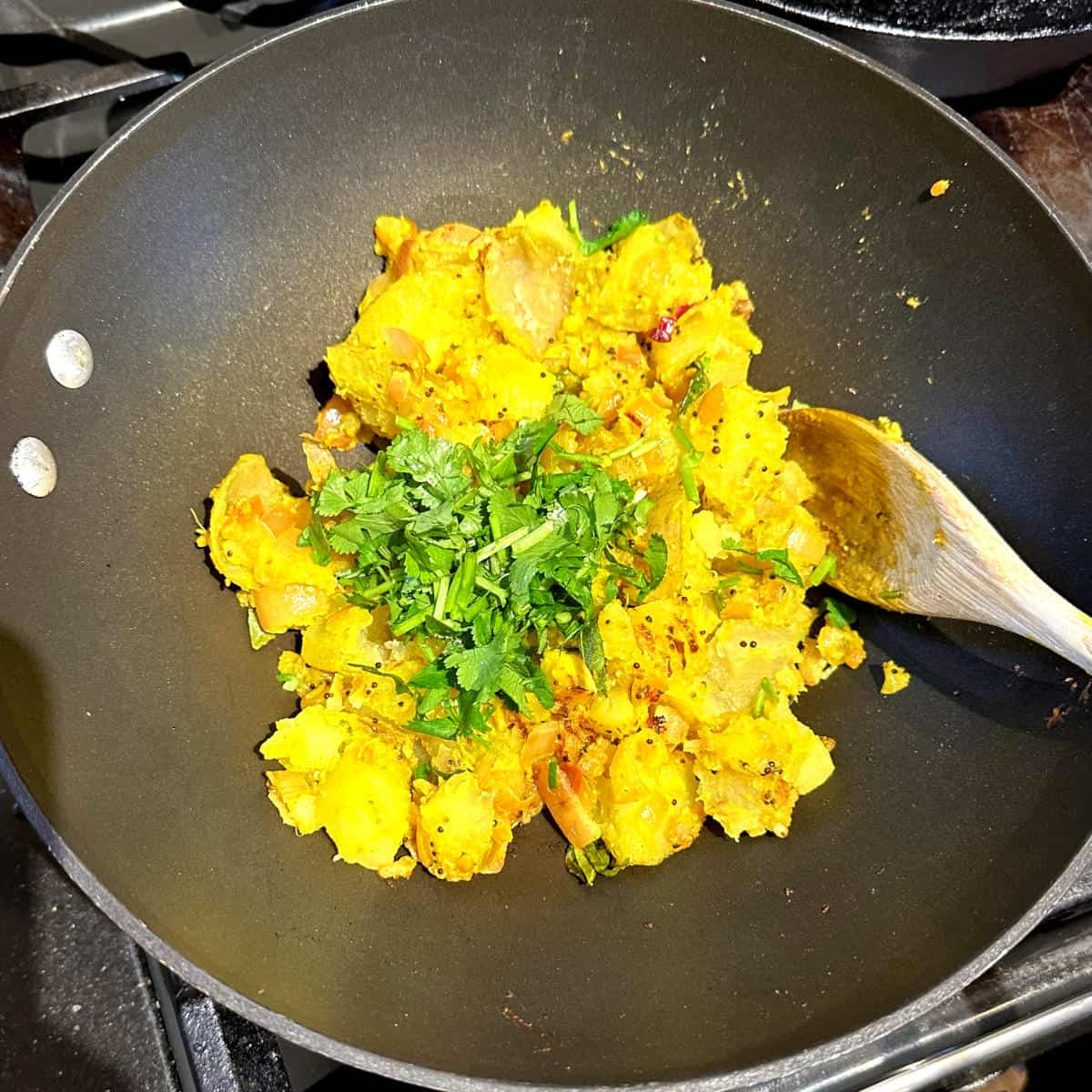 Cilantro added to potatoes in wok.