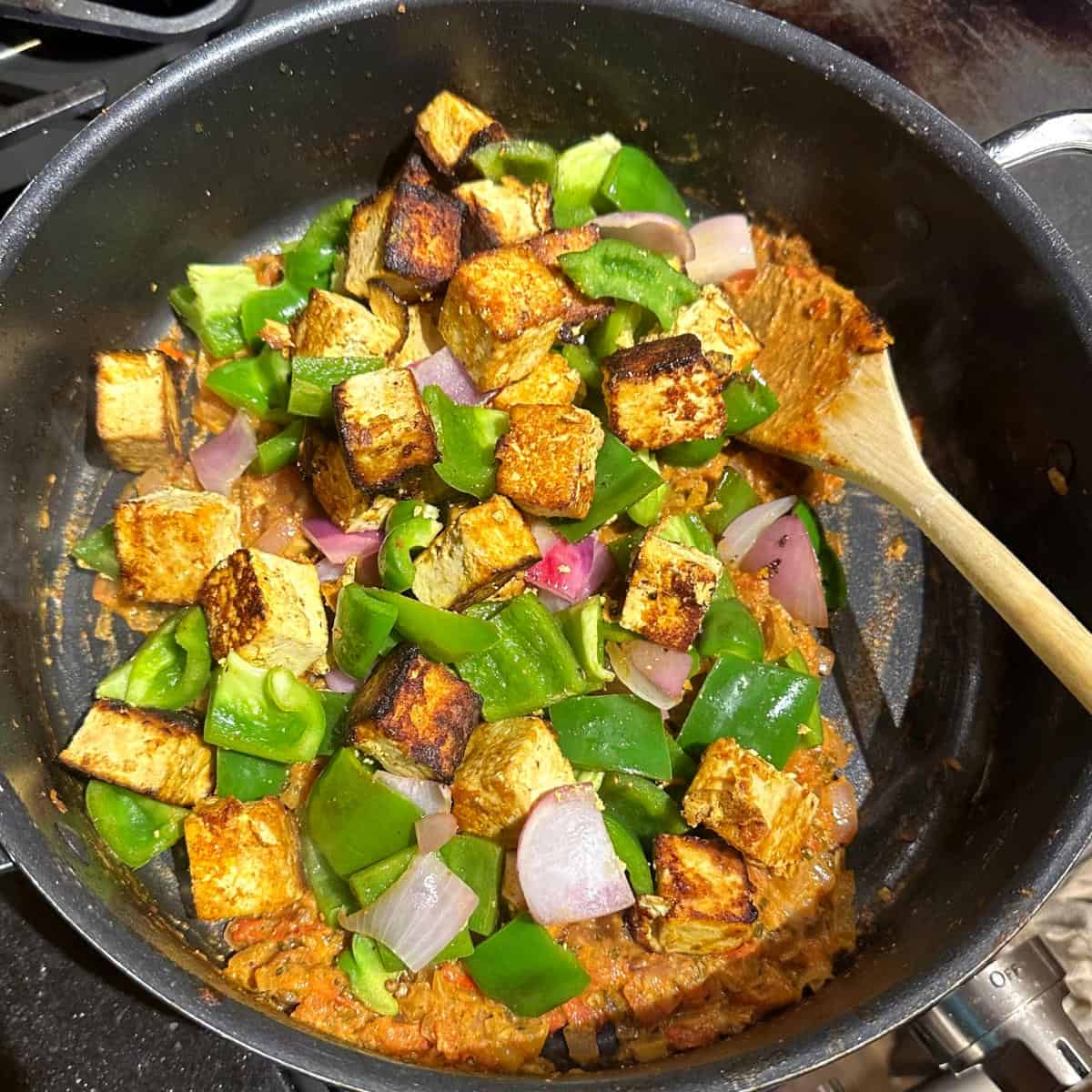 Tofu cubes and bell peppers added to sauce in pan.