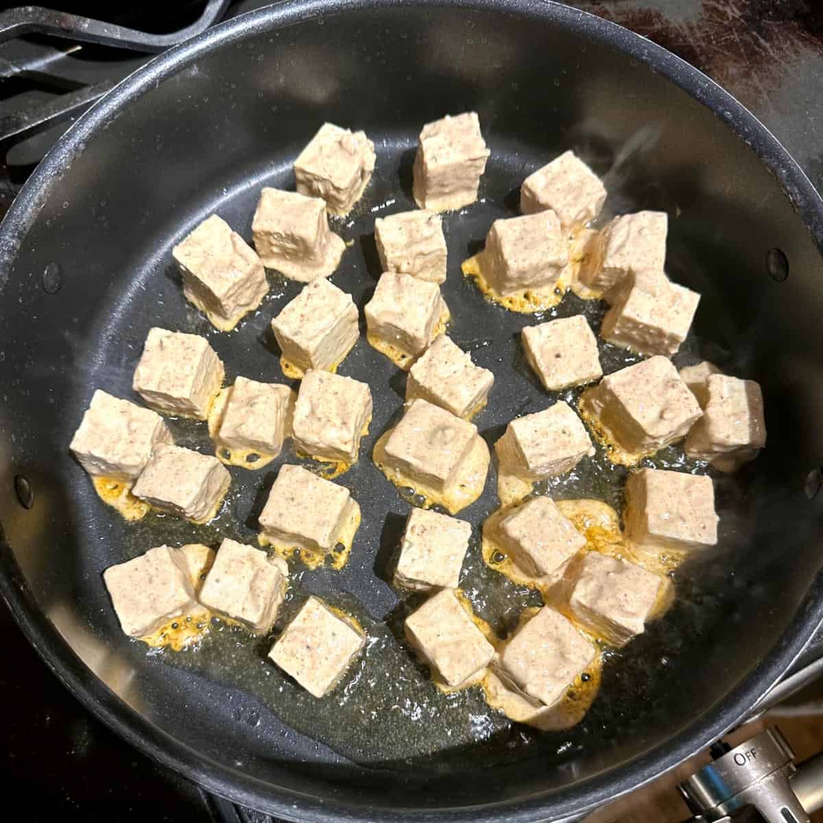 Tofu cubes frying in non-stick pan.