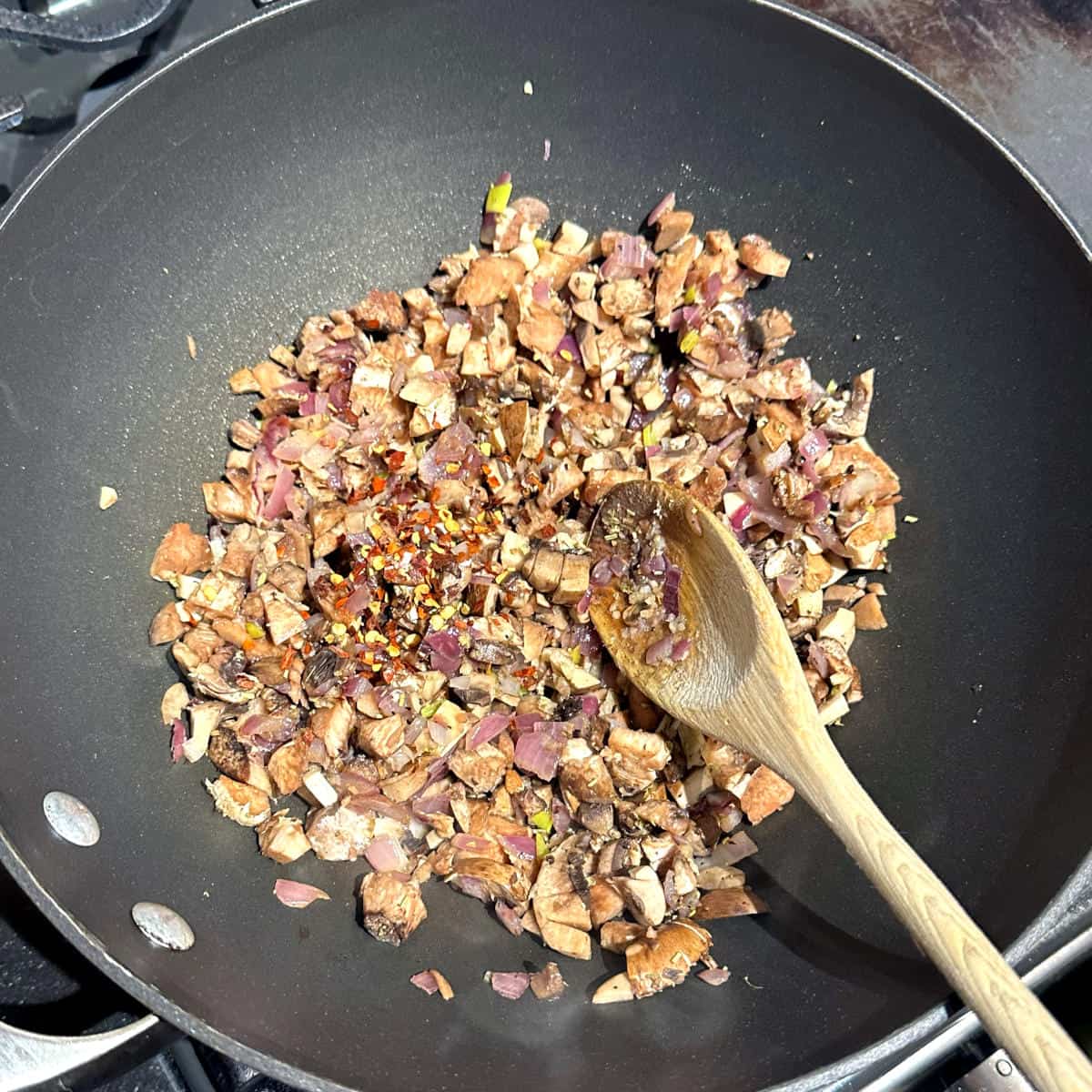 Red pepper flakes added to wok with mushrooms and herbs.