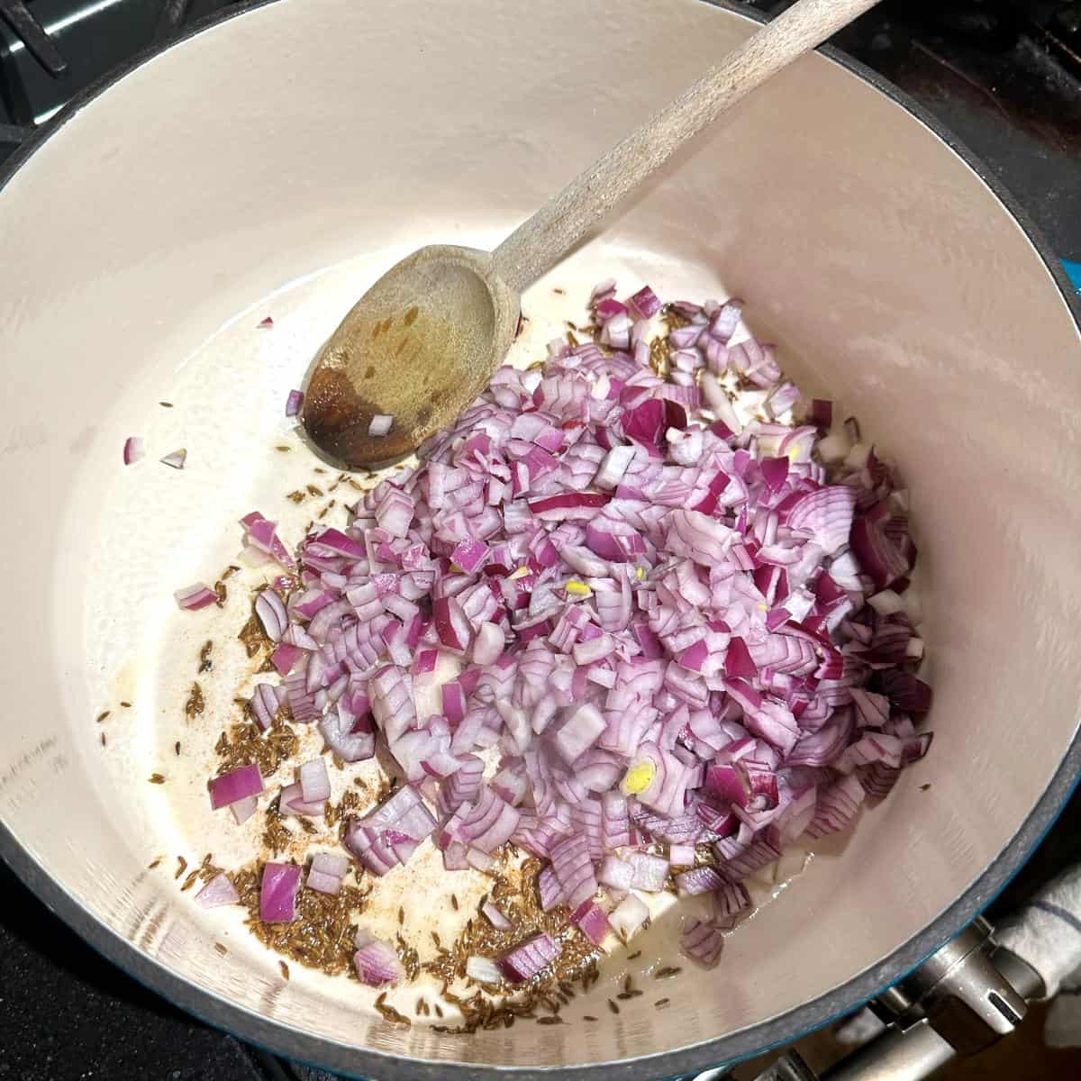 Onions added to cumin seeds in Dutch oven.