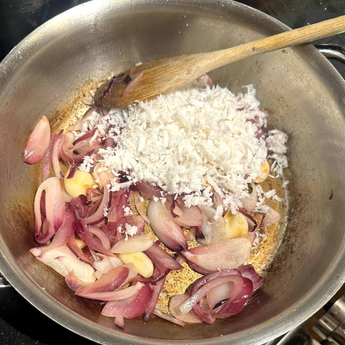 Coconut added to onions and garlic in pan.