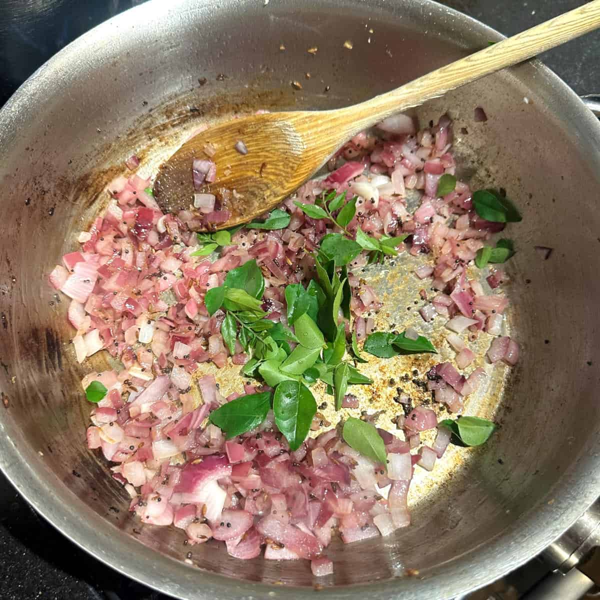 Curry leaves added to onions in pan.