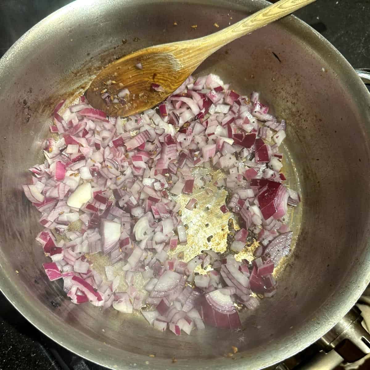 Onions and ginger garlic paste in pot with wooden spoon.