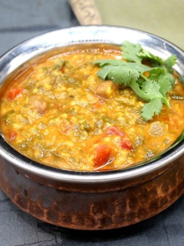 Photo of amaranth dal with cilantro and tomatoes in Indian style copper bowl.