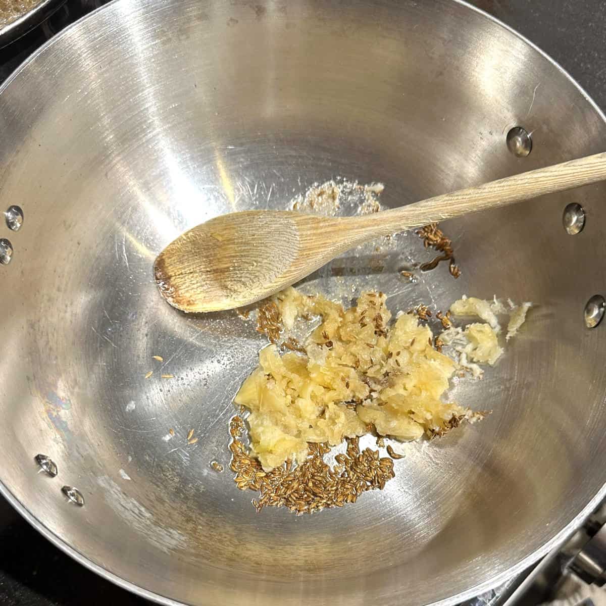 Garlic and cumin seeds frying in pan.