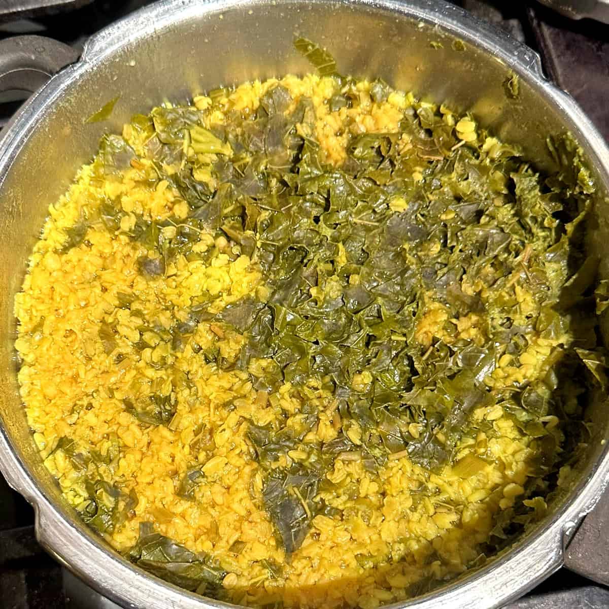 Cooked moong dal and amaranth leaves in pressure cooker pan.