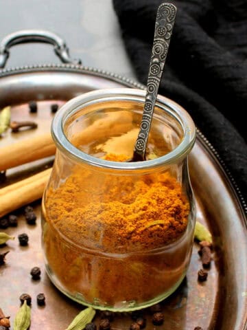 Homemade and authentic Indian style golden milk spice blend in glass jar with spices scattered around.