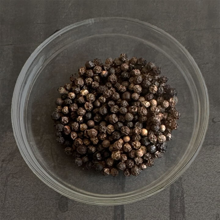 Whole black peppercorns or kali mirch in bowl.