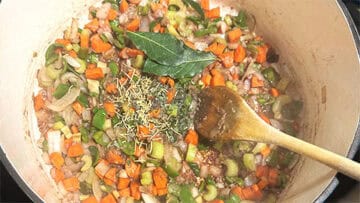 Herbs added to vegetables in pot.