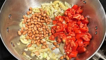 Peanuts and tomatoes added to onions and garlic in saucepan.