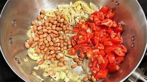 Peanuts and tomatoes added to onions and garlic in saucepan.