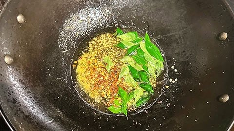 Mustard seeds, urad dal, curry leaves and red pepper in wok.