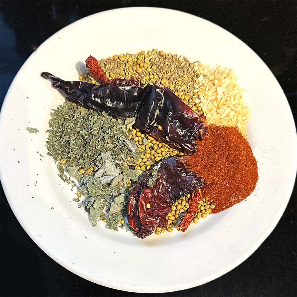 Toasted whole spices on plate with powdered spices and herbs.