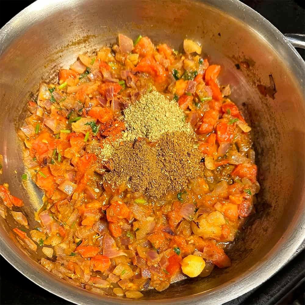 Spices added to tomatoes and onions in pan.