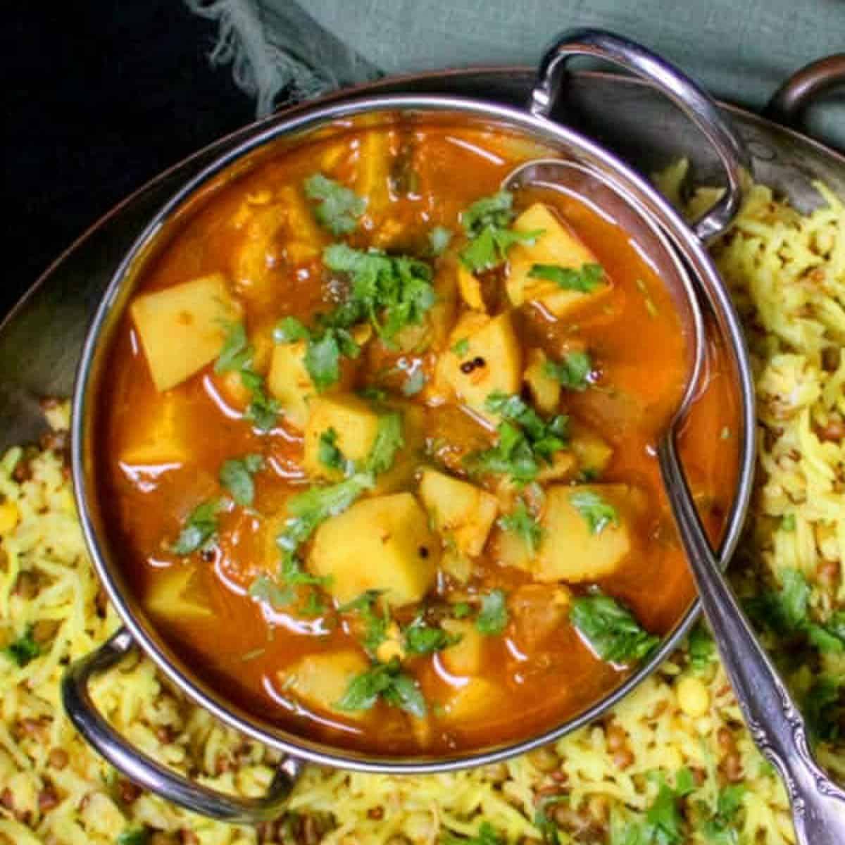 Top down view of potato curry in karahi with khichdi on side.