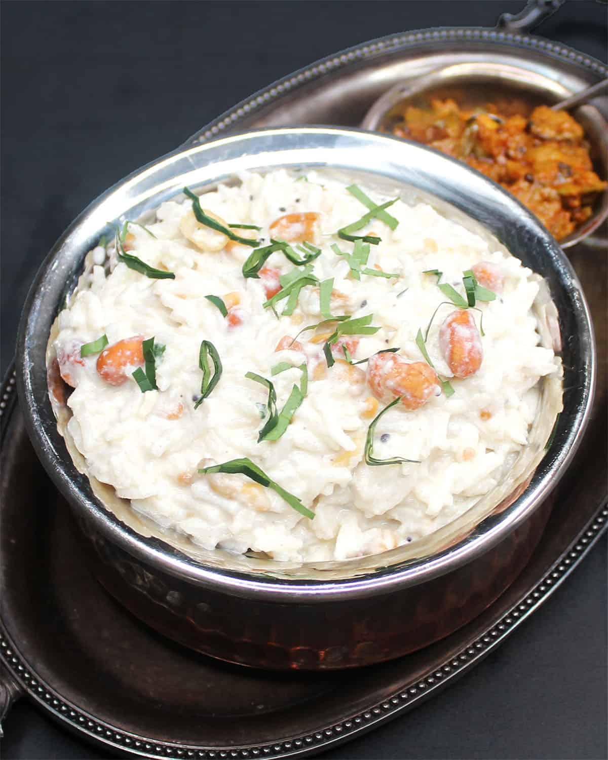 Curd rice in bowl with mango thokku in background.