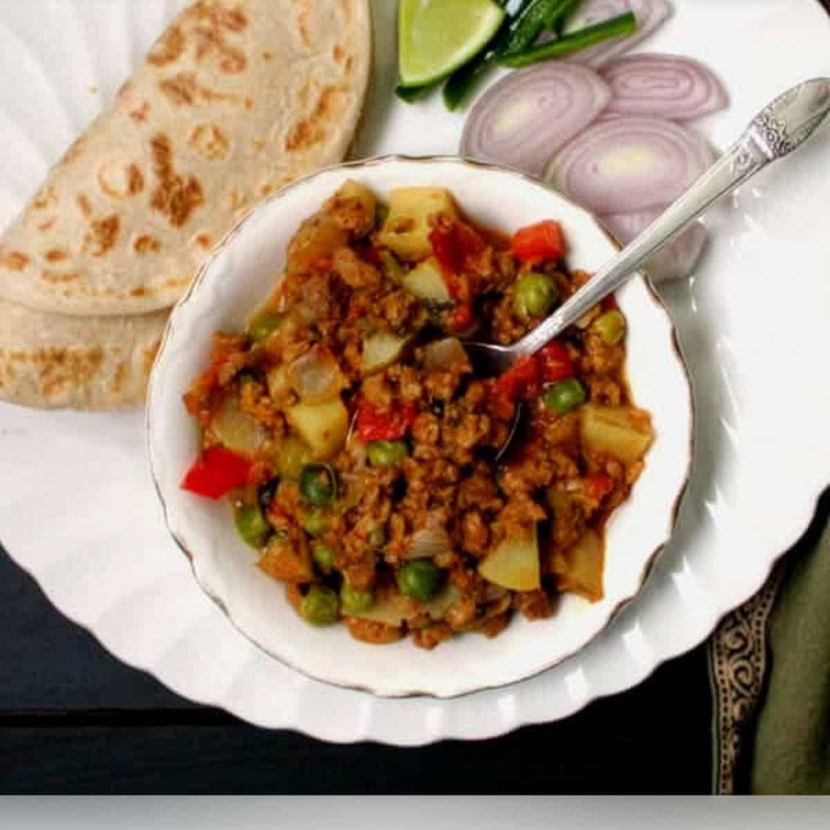 Vegan keema masala in bowl with roti, onions and lime on the side.
