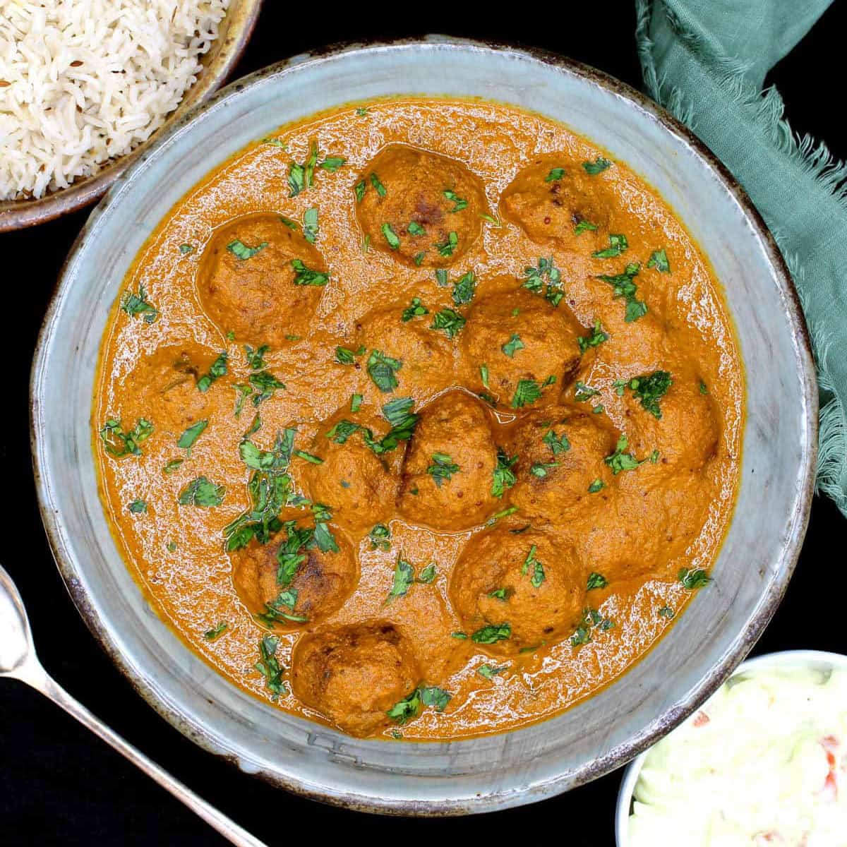 Top down view of vegan meatball curry with rice on side.