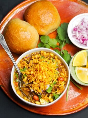 Misal pav in clay platter with onions, lemons and cilantro on the side.