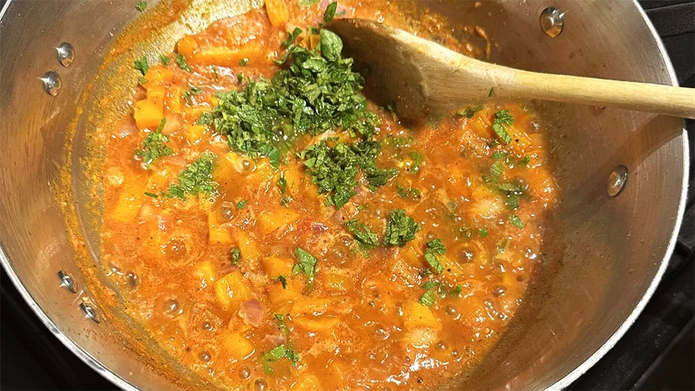 Herbs added to tomatoes and veggies in pan.