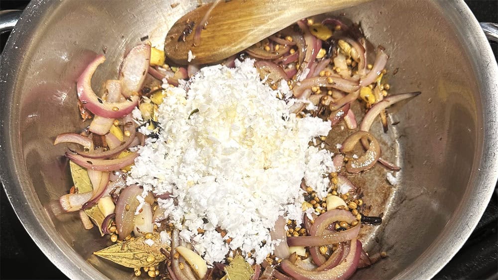 Coconut added to spice in pan.