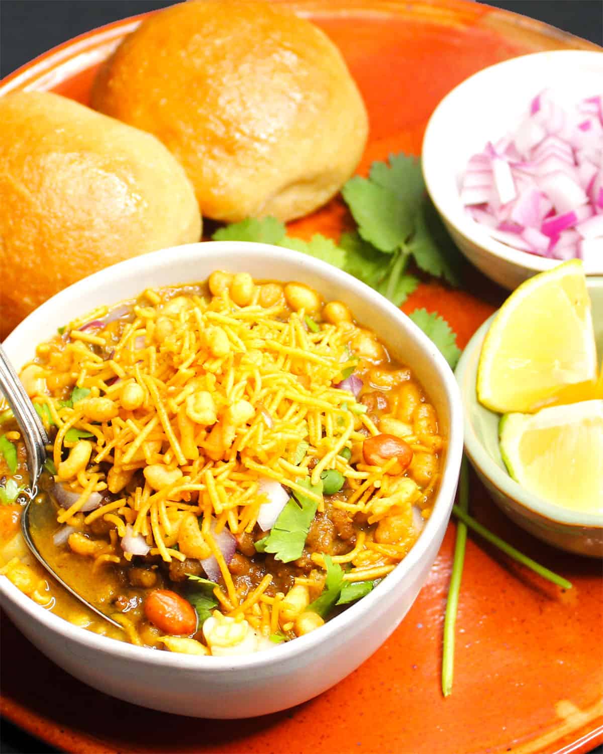 Front shot of misal pav with lemon wedges, cilantro and onions.