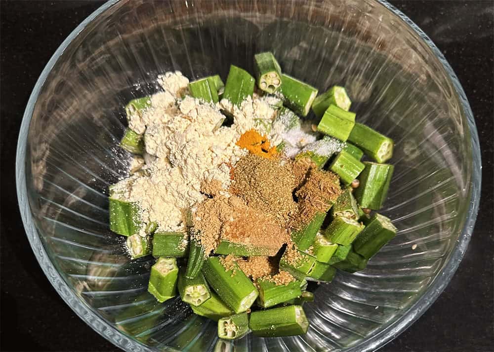 Spices and chickpea flour added to okra in bowl.