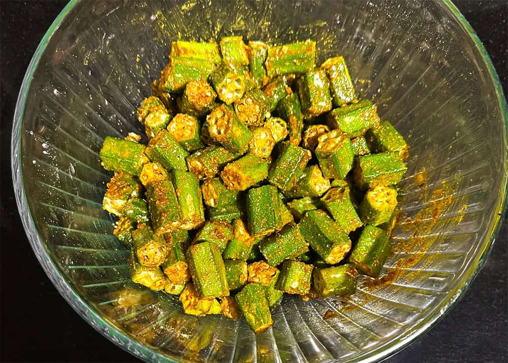 Okra tossed with spices and oil in bowl.