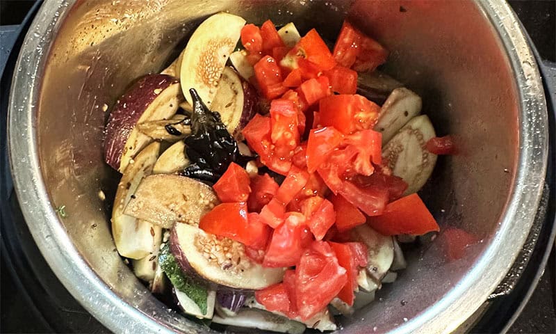Eggplant and tomatoes added to tempering in pot.