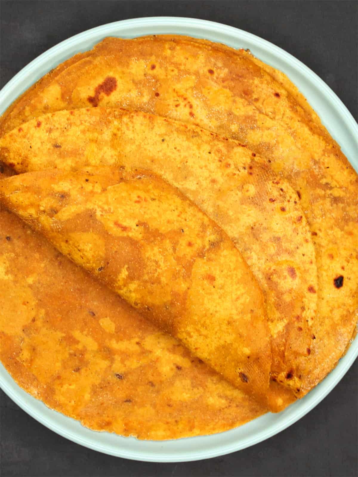 Overhead view of soft pumpkin parathas on plate.