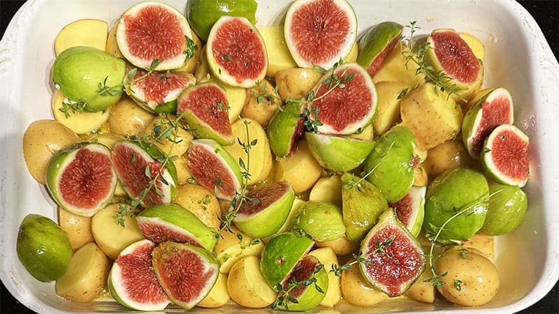 Figs and potatoes with dressing and thyme in baking dish.